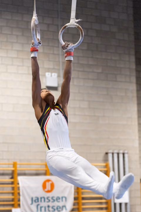 Gymnast performing a suspended hold on still rings with extended body position, showing strength and control in training facility