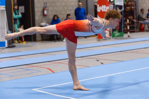 Young gymnast holds an arabesque position on floor mat, extending leg and arms with focused concentration during routine
