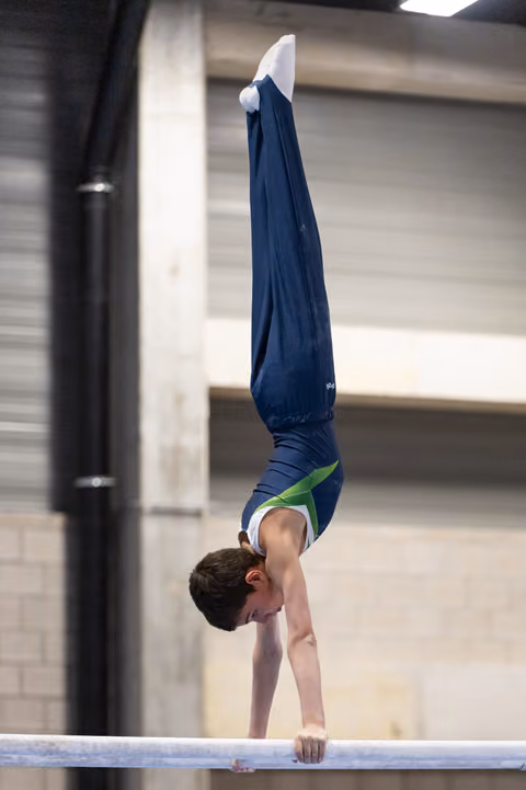 Young male gymnast performs a vertical handstand on the balance beam, demonstrating strength and precision in an indoor training facility