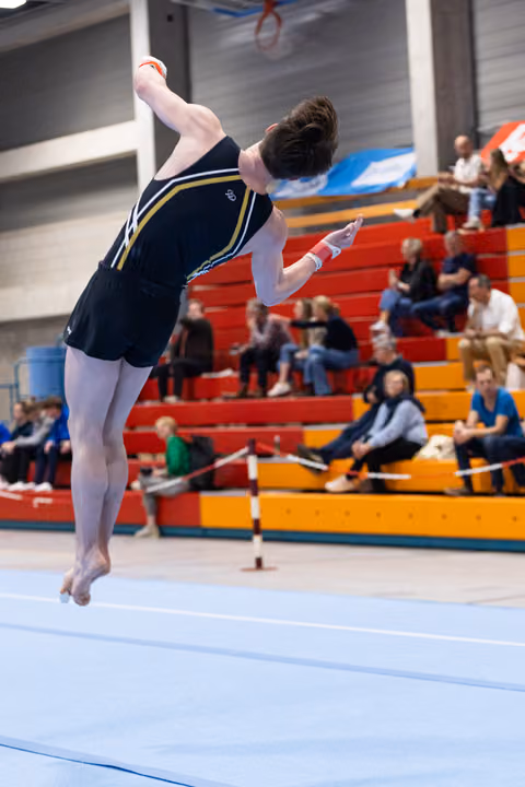 Gymnast executes dynamic tumbling pass with arched back mid-air on floor exercise in gymnasium competition