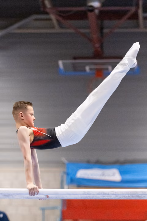 Young male gymnast executes a horizontal hold on parallel bars, legs extended upward, displaying strength and control