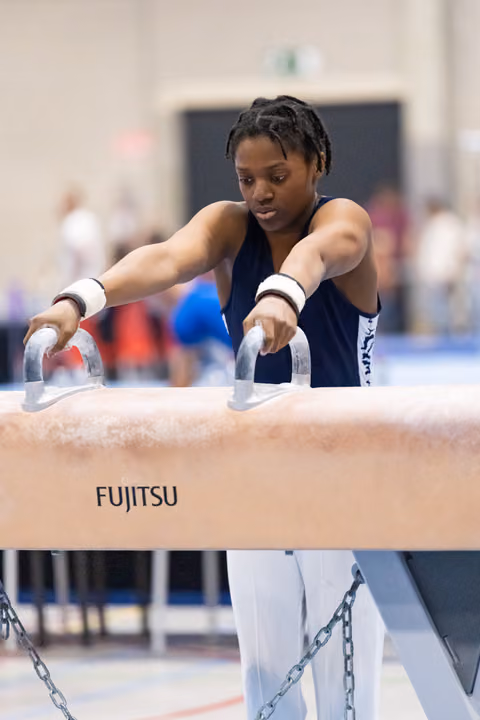 Female gymnast grips pommel horse handles with intense concentration during routine at Fujitsu-sponsored event