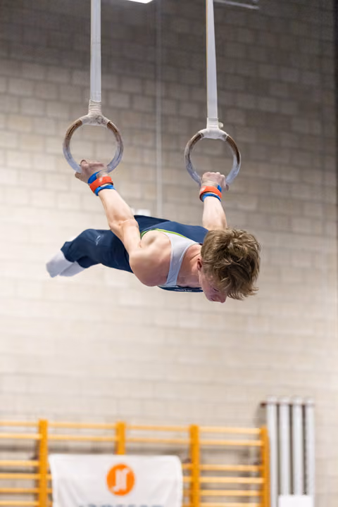 Young gymnast performing an iron cross hold on gymnastics rings, displaying remarkable strength and control in the gym