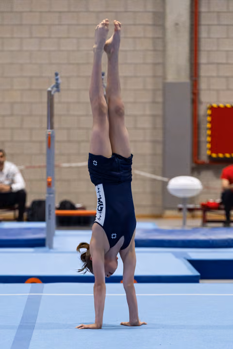 Young gymnast performs handstand on floor exercise mat, demonstrating strength and balance during training session