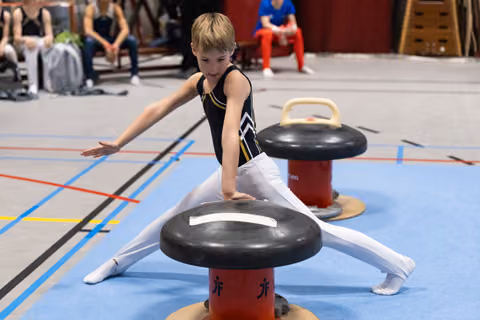 Young gymnast performs splits on red mushroom apparatus, concentrating on form with arms extended during training