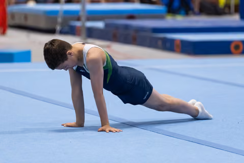 Young male gymnast holds a plank position on blue floor mat, demonstrating strength and concentration during training