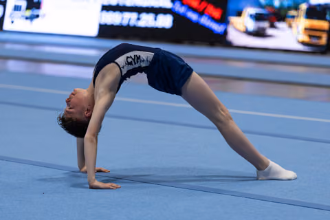 Young gymnast executes a deep backbend bridge position during floor routine, demonstrating exceptional flexibility and control