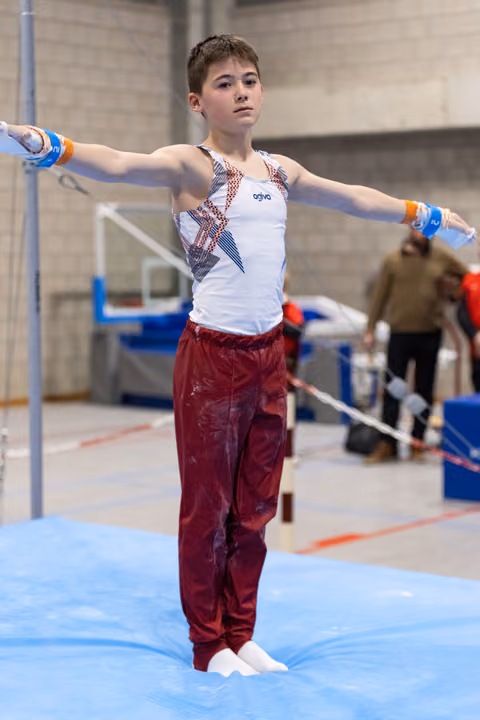 Young gymnast performs on parallel bars with extended arms, wearing maroon pants and white leotard in training facility