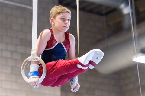 Young gymnast performing on rings with extended legs, demonstrating strength and control during routine