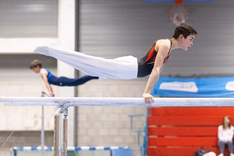 Young male gymnast holds a horizontal position on parallel bars during training, displaying strength and control