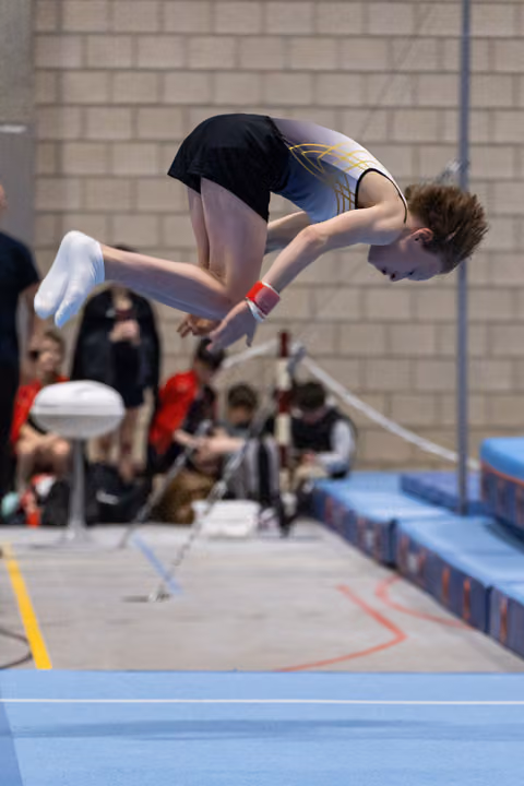 Gymnast performs inverted somersault over vault table, body tucked tightly in mid-air during indoor gymnastics event