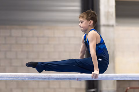 Young gymnast holds an L-sit position on the horizontal bar, demonstrating strength and control during his routine