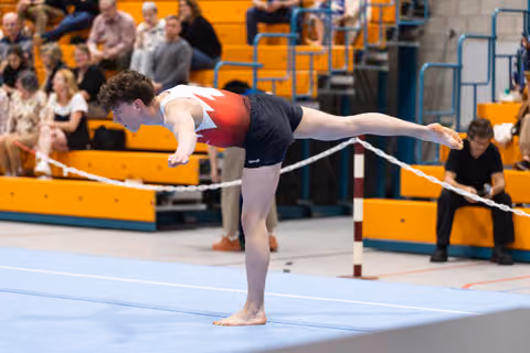 Young gymnast performs a horizontal scale balance on the beam, body fully extended parallel to the apparatus during routine