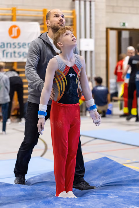 Young gymnast in red pants and coach both looking upward attentively during training in indoor gymnasium