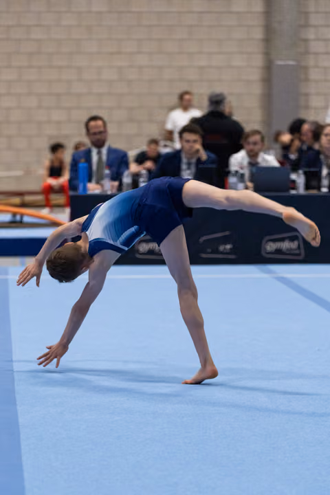 Gymnast performs graceful backbend during floor exercise, arching backwards with hands reaching toward mat