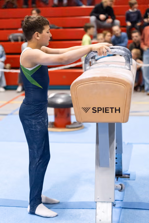 Young gymnast in navy leotard positions hands on Spieth pommel horse, focused and ready before routine in competition venue