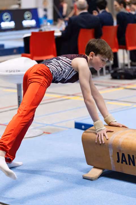 Young gymnast in orange pants holds a plank position on the pommel horse during training, focused and determined