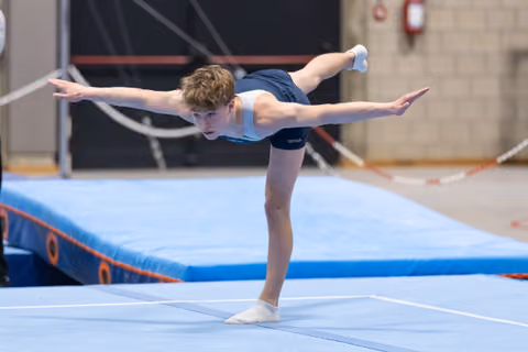 Young gymnast performs graceful balance pose with extended leg and arms on floor mat in training facility