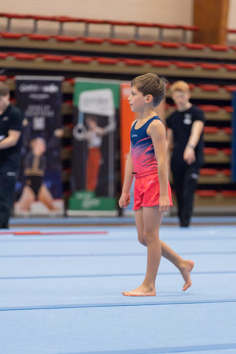 Young male gymnast walks barefoot across the blue floor mat, composed and focused before his routine.
