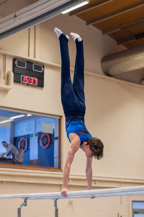 Young male gymnast holds a perfect handstand on parallel bars, legs straight up, in an indoor gymnasium.