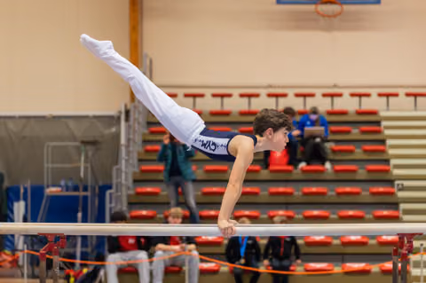 Young male gymnast executes a precise horizontal hold on parallel bars, body perfectly parallel to the ground in a competitive gym.