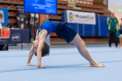 Young gymnast performs a back bridge position on the floor mat during a gymnastics meet, head inverted, focused.