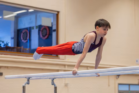 Focused boy performing a planche hold on parallel bars, body perfectly horizontal, showing strength and concentration.