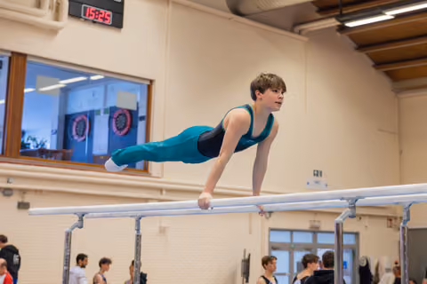 Young gymnast holds a focused planche position on parallel bars, body horizontal, determined expression in a gymnasium.