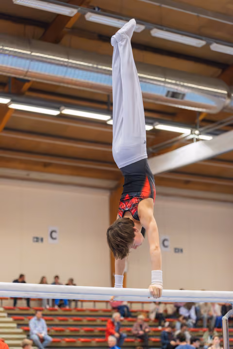 Young male gymnast performs a perfect handstand on parallel bars, body fully extended, in an indoor gymnastics hall.