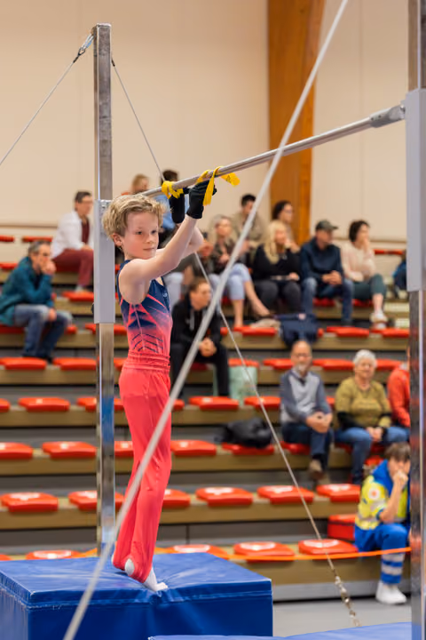 Focused young male gymnast grips the high bar with determination, standing on a blue mat block before his routine.