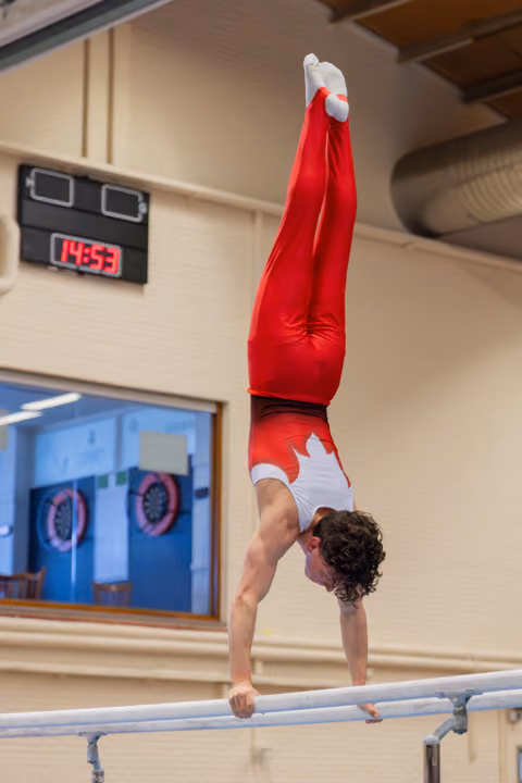 Canadian gymnast performs a perfect handstand on parallel bars, body fully extended and legs pointing upward.