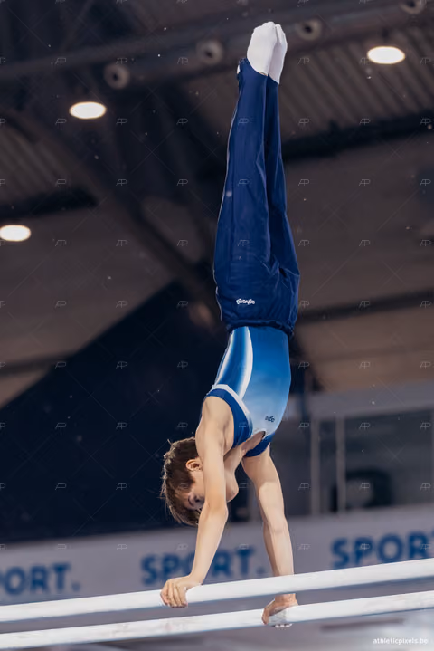Young male gymnast performs a perfect handstand on parallel bars, body fully extended, in a sports hall.