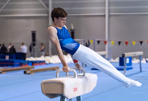 Young male gymnast performing horizontal hold on pommel horse with focused expression during training session