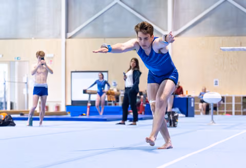 Young male performer executes floor routine with extended arms and focused expression in indoor sports facility