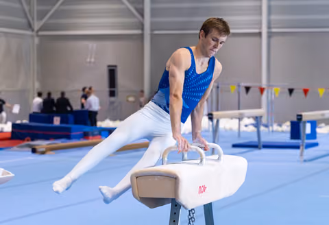 Young male gymnast performing a leg extension on pommel horse during training, demonstrating strength and balance