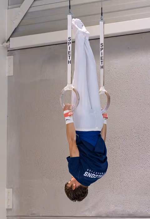 Young athlete hanging upside down on still rings, demonstrating strength and body control during training