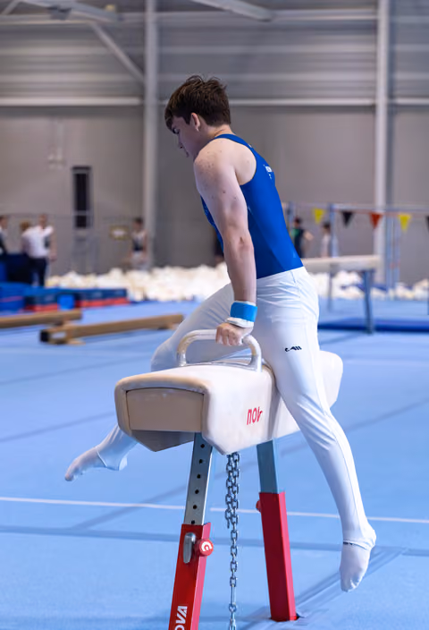 Male gymnast in blue and white uniform practicing on pommel horse in indoor training facility
