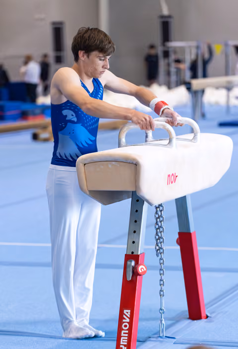 Young male gymnast adjusting hand grips on pommel horse before routine in training facility