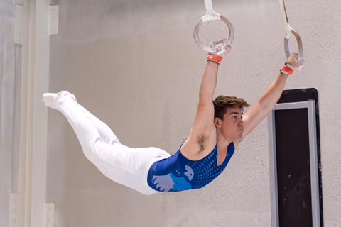 Young male gymnast performing an iron cross hold on still rings, displaying strength and concentration in a training facility