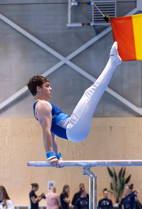 Male gymnast performs impressive V-sit hold on parallel bars during routine, demonstrating exceptional core strength and control
