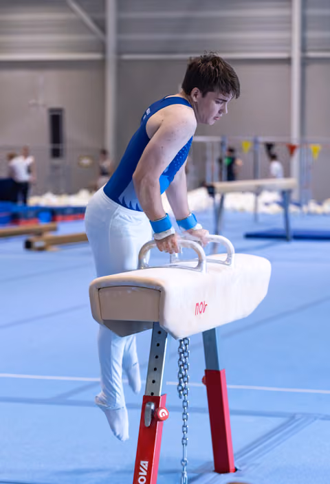 Male gymnast executes a move on the pommel horse, displaying concentration and strength in a training facility