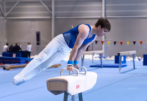 Male gymnast performing horizontal plank hold on pommel horse, demonstrating strength and control in training facility