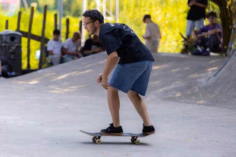 Man skateboarding through a park pathway, crouched in concentration with spectators watching in the background