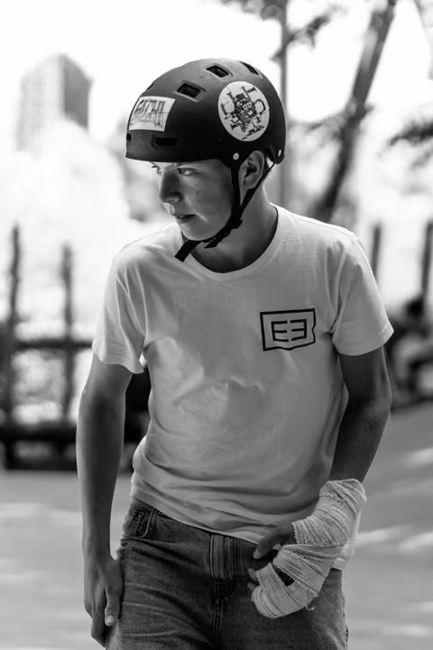 Young athlete wearing protective helmet and bandaged hand, gazing to the side with focused expression at outdoor venue