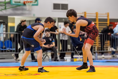 Two young wrestlers in aggressive stance facing each other intently on a colorful mat during an indoor tournament.
