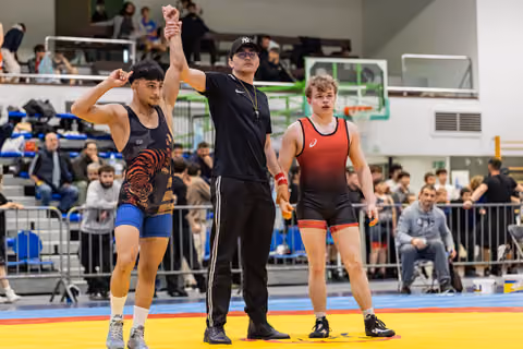 Referee raises the arm of a victorious wrestler in a tiger singlet; the defeated opponent stands quietly beside them.