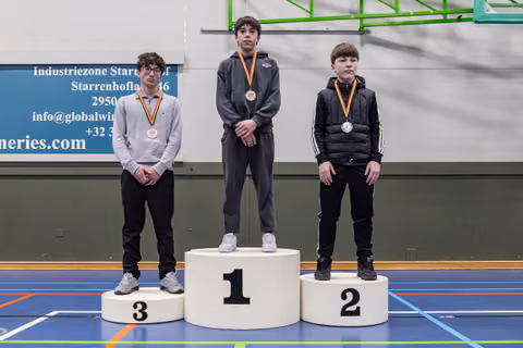 Three young male athletes stand on a podium, 1st place center with gold medal, 2nd and 3rd with silver and bronze, in a gym.