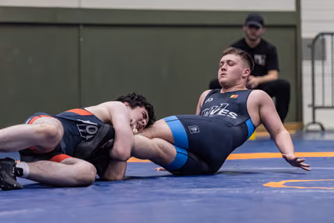 Young wrestler being pinned on his back while opponent maintains control, referee watching closely in background.