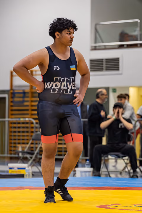 Young wrestler in Wolves singlet stands confidently with hands on hips, surveying the mat during a wrestling event.