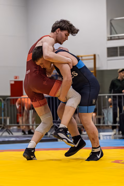 Two young wrestlers locked in a fierce clinch on a yellow mat, straining with intense effort during an indoor tournament.